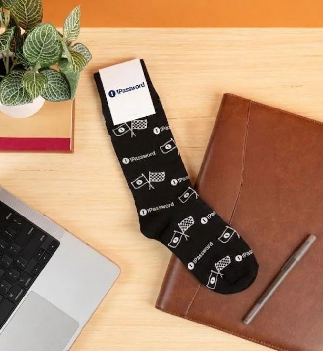 Finished black 1Password custom sock displayed beside a laptop and notebook