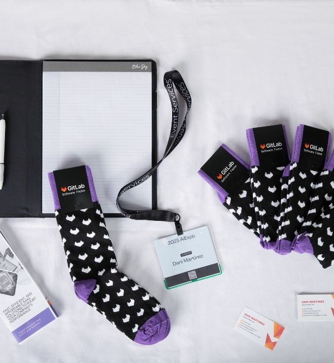 GitLab conference socks displayed beside an attendee badge and notebook