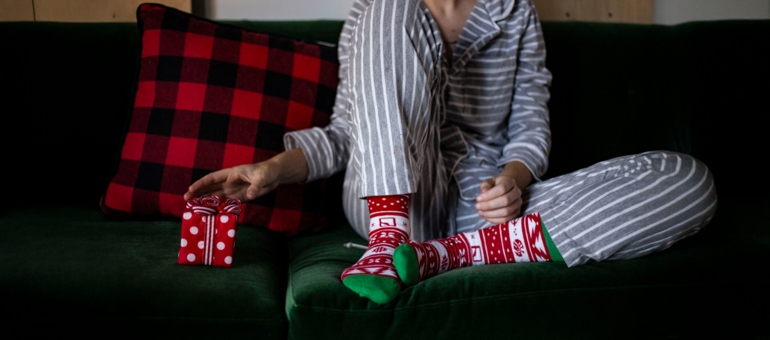 Person in striped pajamas wearing red and green holiday socks beside a small wrapped gift