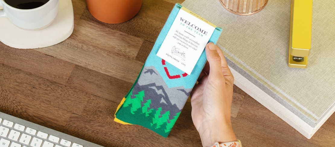 New employee holding custom socks and a welcome card at a desk