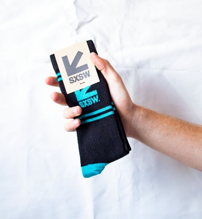Hand holding black and turquoise SXSW socks with a custom header card