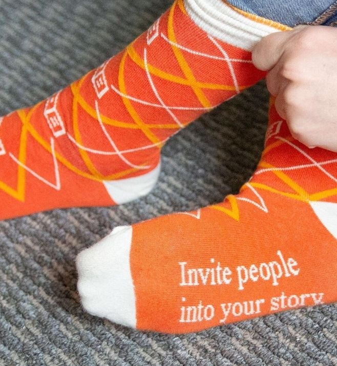 Orange custom socks with the message Invite people into your story