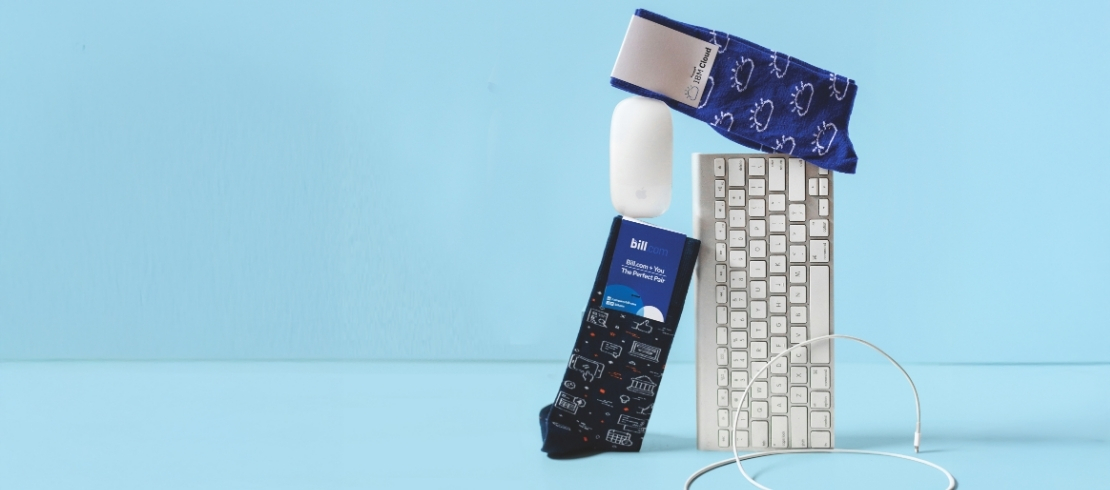 Custom tech conference socks displayed with a keyboard, charger, and cables