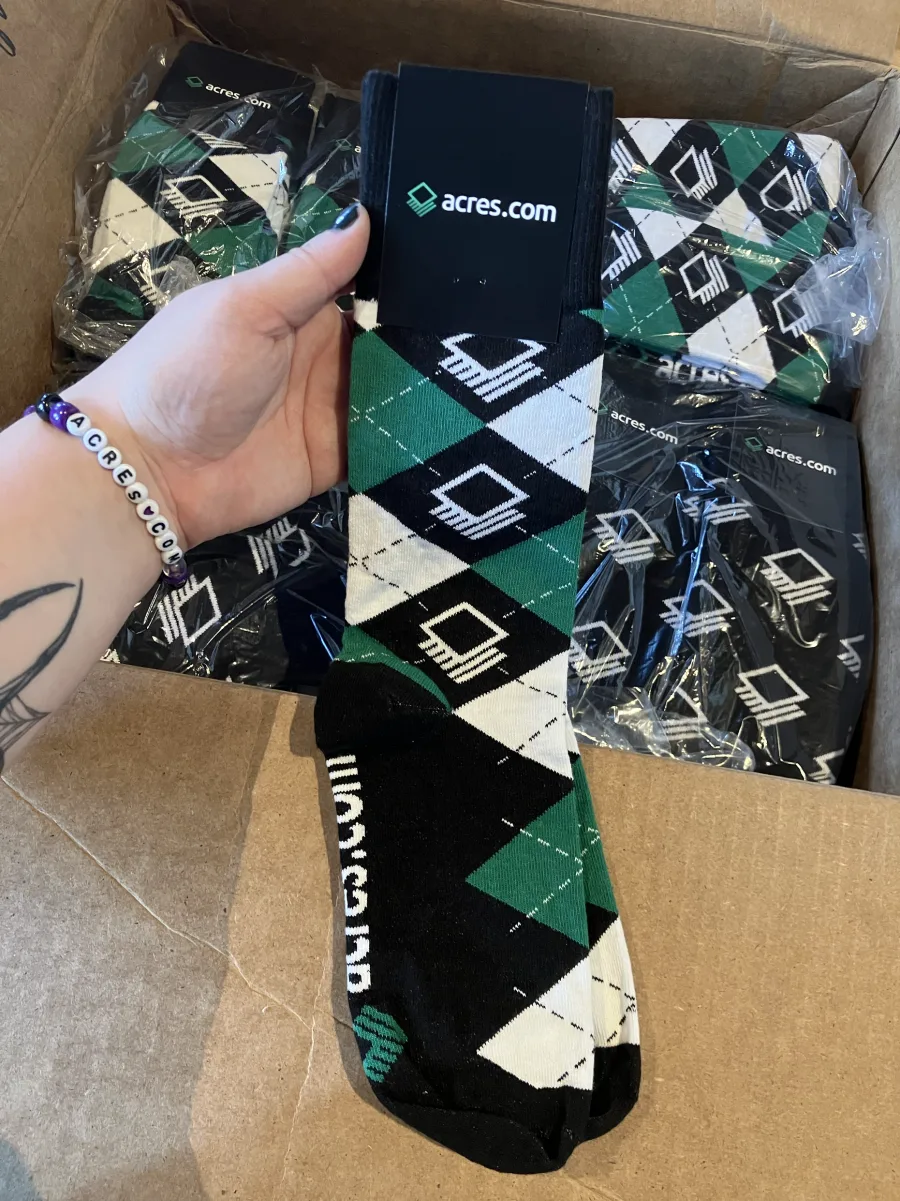 Green, black, and white Acres custom socks with branded packaging